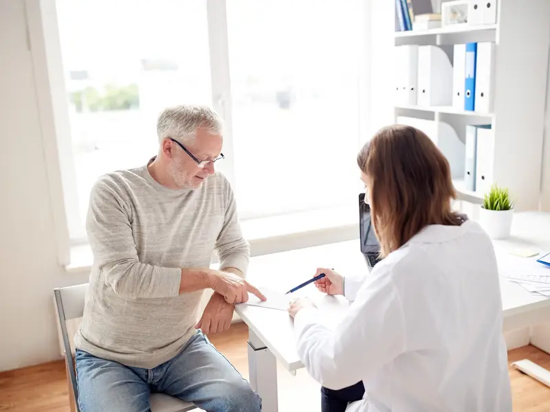 Female healthcare provider sitting with male patient at an office desk, explaining how to prepare for a sigmoidoscopy.