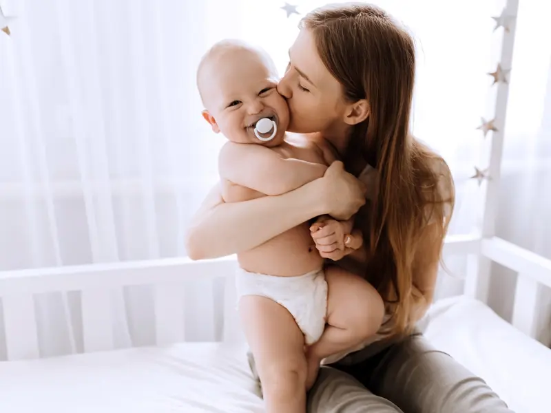 A mother embraces her baby and kisses them on the cheek