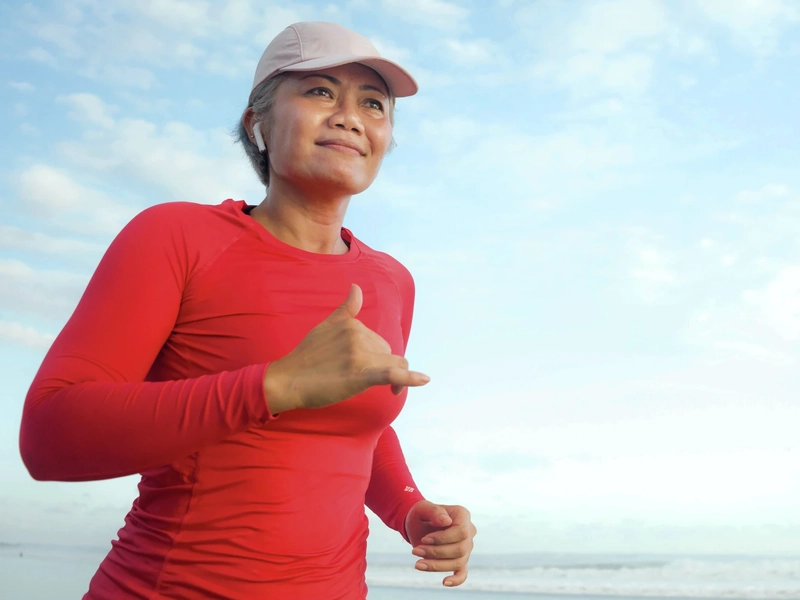 A woman wearing a red shirt with a hat runs by a body of water