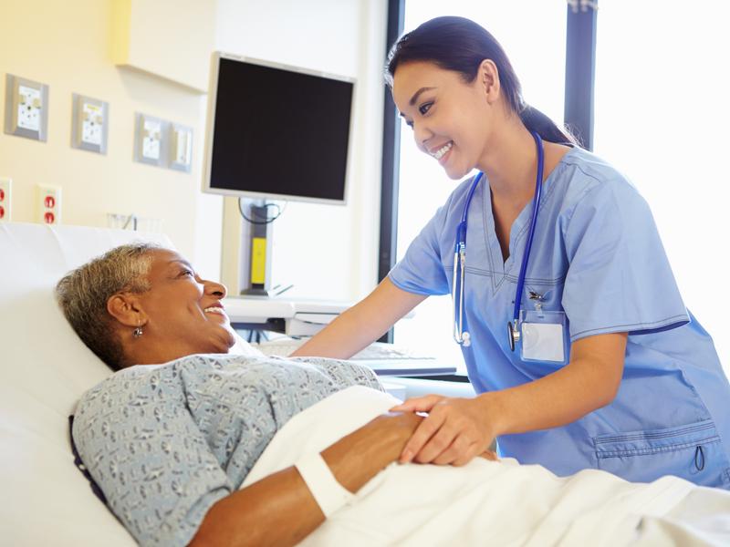 Cardiologist smiling and reassuring older female patient lying in a hospital bed after an interventional cardiology procedure