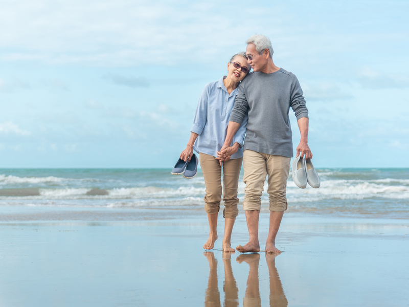 Older couple walking on the beach holding hands after receiving orthopedic care