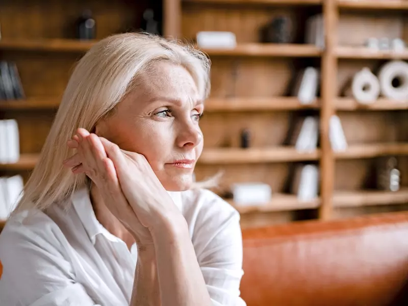 Woman with post-traumatic stress disorder sitting on a couch, gazing off-camera with her hands near her face