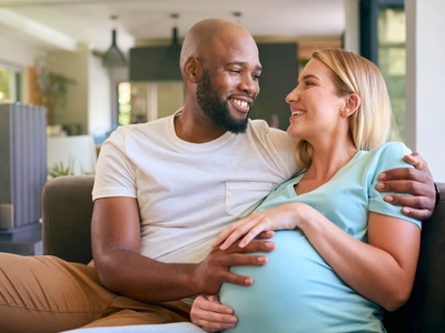 A pregnant woman with high-risk pregnancy and her partner sitting on a couch 