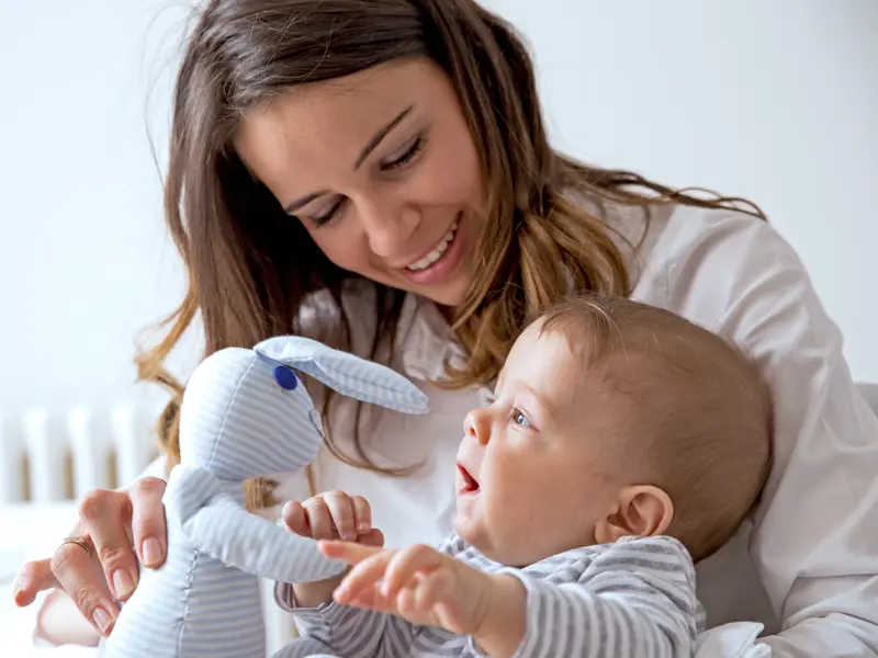 mother showing young infant a stuffed bunny rabbit and smiling