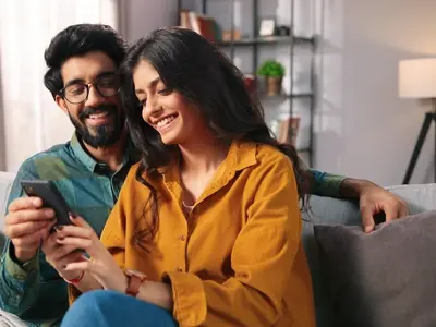 A couple sitting on a couch, smiling while researching iui vs ivf on a smartphone together