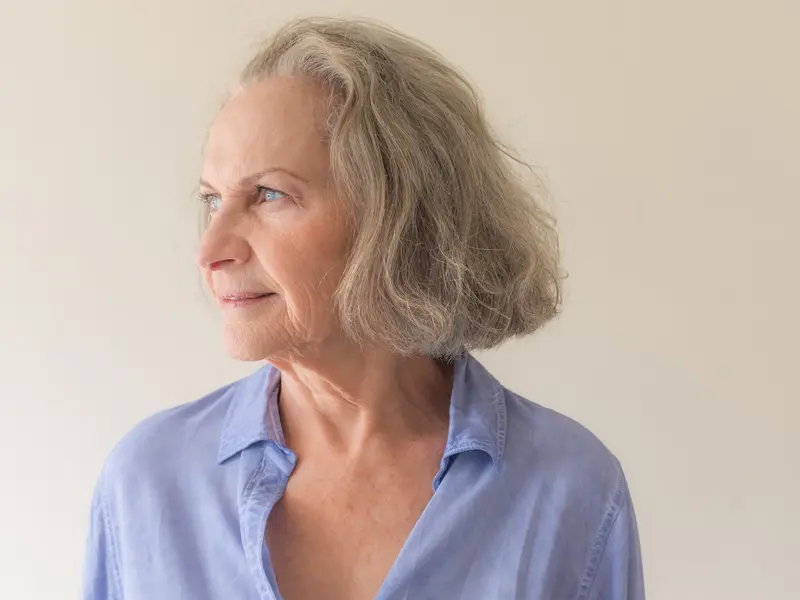 older woman looking off to the right side standing in front of plain wall