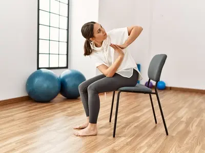 woman sitting on a chair inside practicing chair yoga for its health benefits