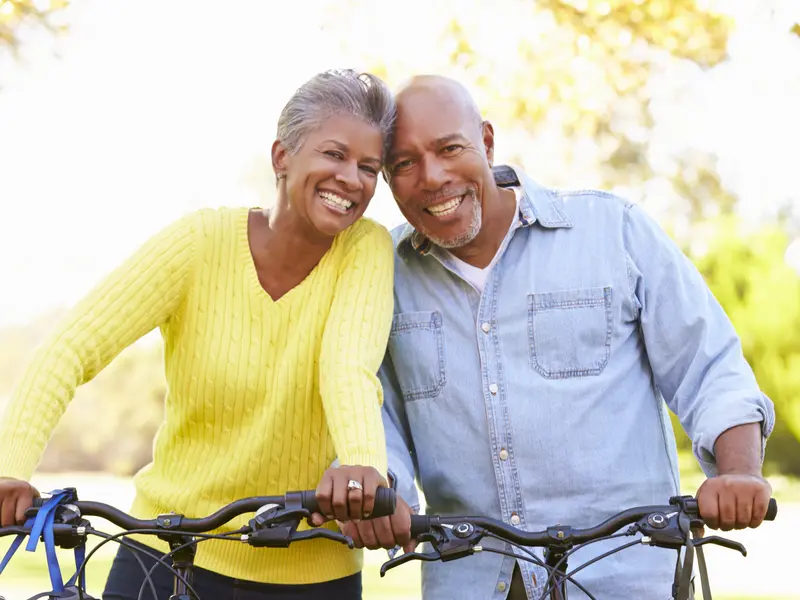 happy couple with head together, smiling at camera while riding bicycles on sunny day outside