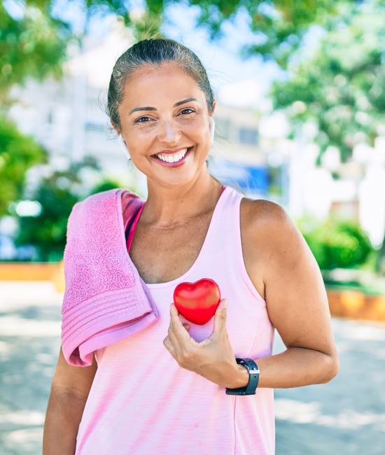 woman outside on sunny day holding red heart up to chest symbolizing heart health
