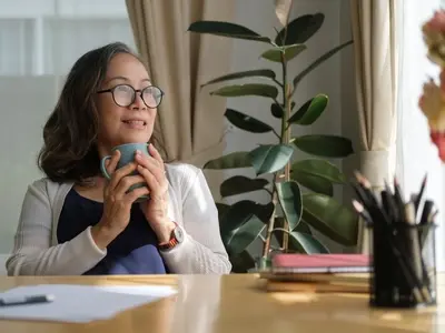 Una mujer se sienta en una ventana tomando una taza de café, sintiéndose descansada y tranquila después de reconocer los signos de agotamiento.