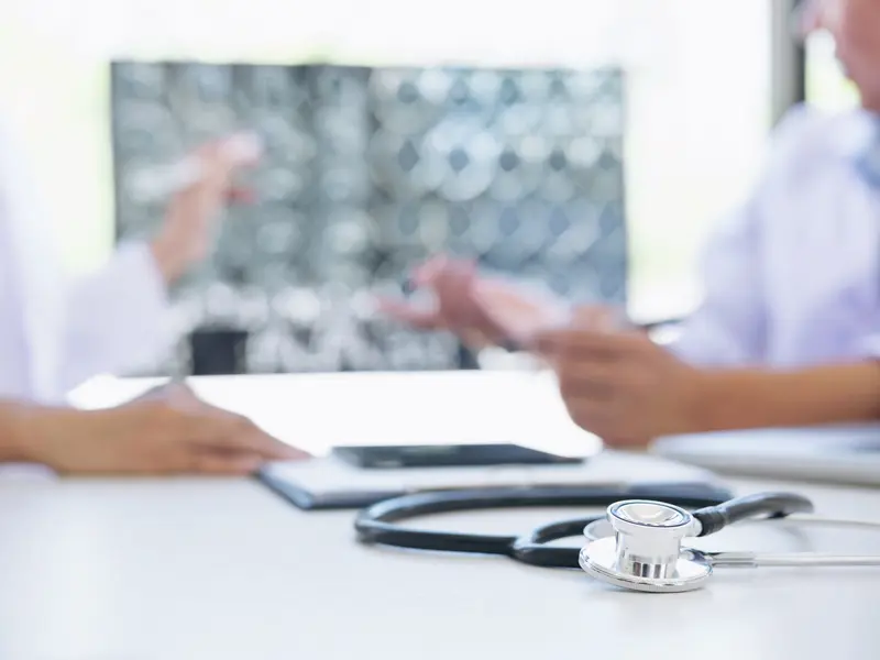  Two neurologists reviewing a patient's brain tumor scan, with a stethoscope in focus and the scan blurred in the background.