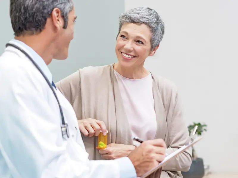 Male oncologist explaining brachytherapy side effects to a female patient, who smiles at the doctor while holding a medication bottle.