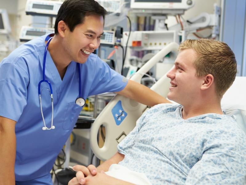 Vascular surgeon smiling and reassuring a patient sitting up in a hospital bed, confirming the success of the vascular surgery