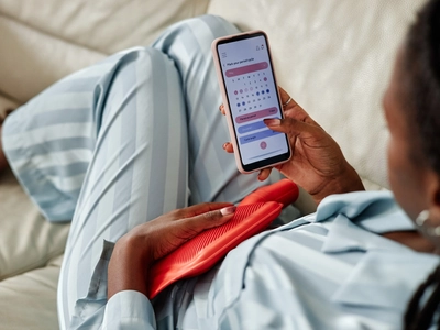 Una mujer mira la aplicación de su ciclo menstrual en su teléfono para entender si está experimentando síntomas del síndrome premenstrual (SPM) o del embarazo