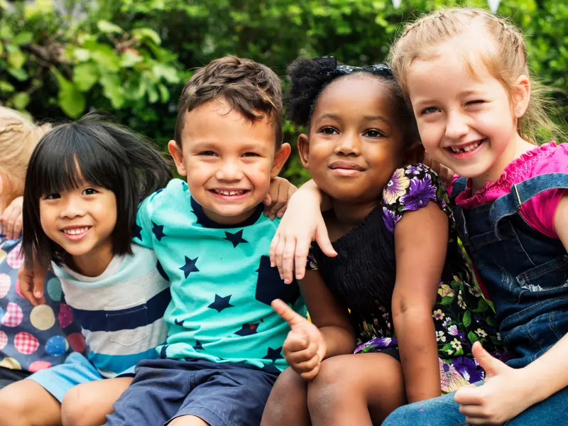 group of young children of different ethnicities sitting and smiling at camera in front of trees