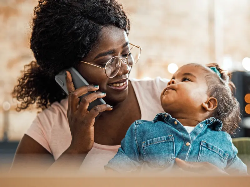 young toddler girl looking up at her mother wearing glasses talking on the phone and smiling at child