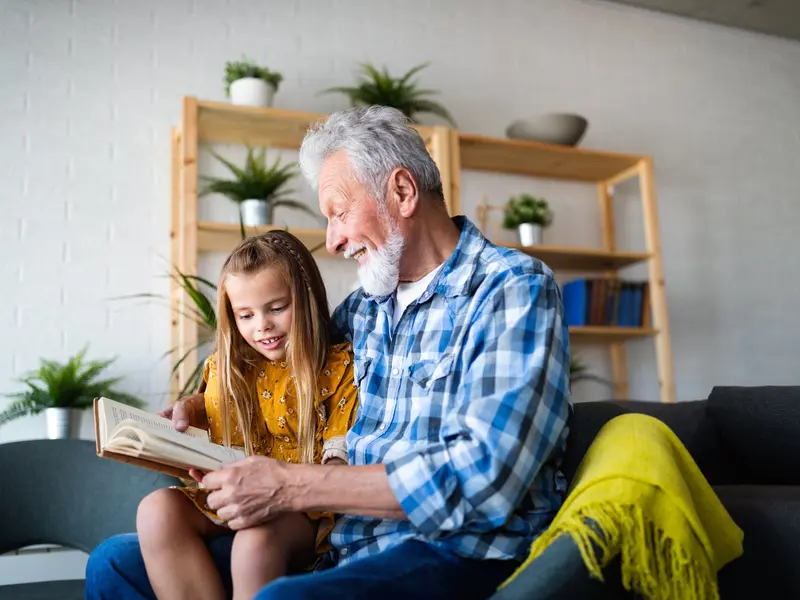 grandfather living with congenital heart disease sitting on couch reading to young granddaughter