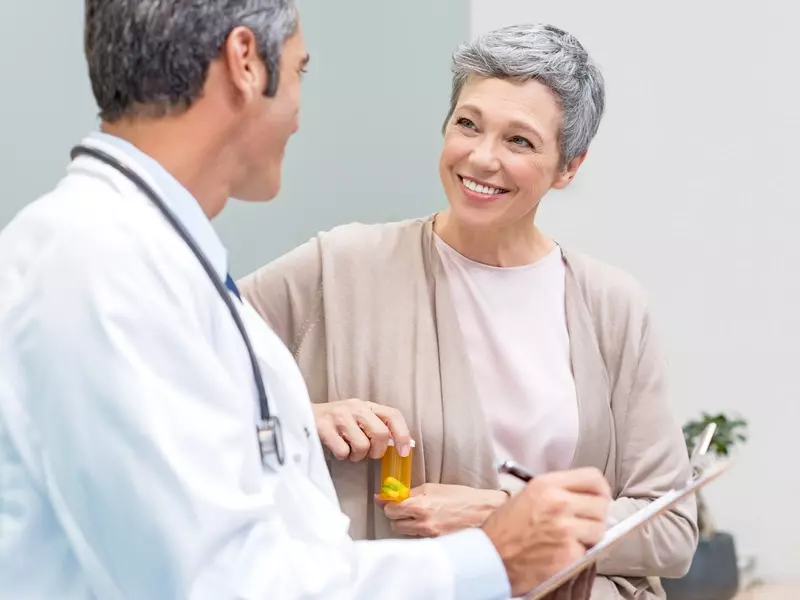 Vascular surgeon holding a clipboard, smiling at a female patient with carotid artery disease who is holding a medication bottle