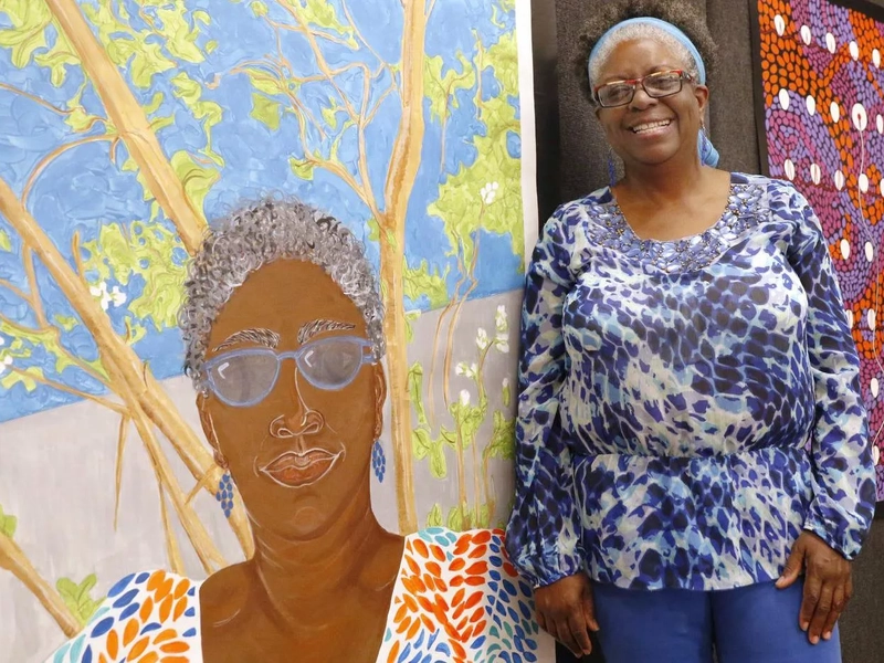 A heart arrhythmia patient stands next to a large canvas displaying her work.