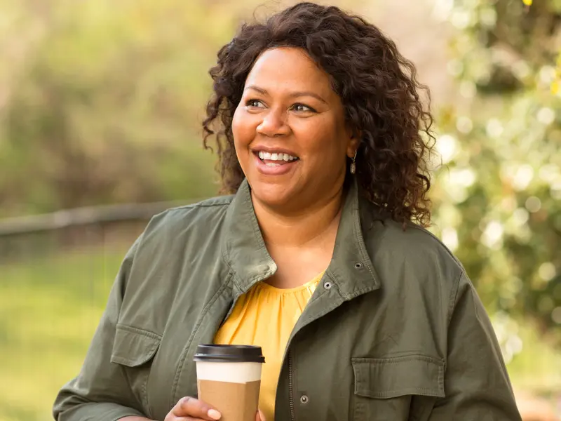 woman holding cup of coffee outside on a sunny after a non-invasive cardiovascular procedure