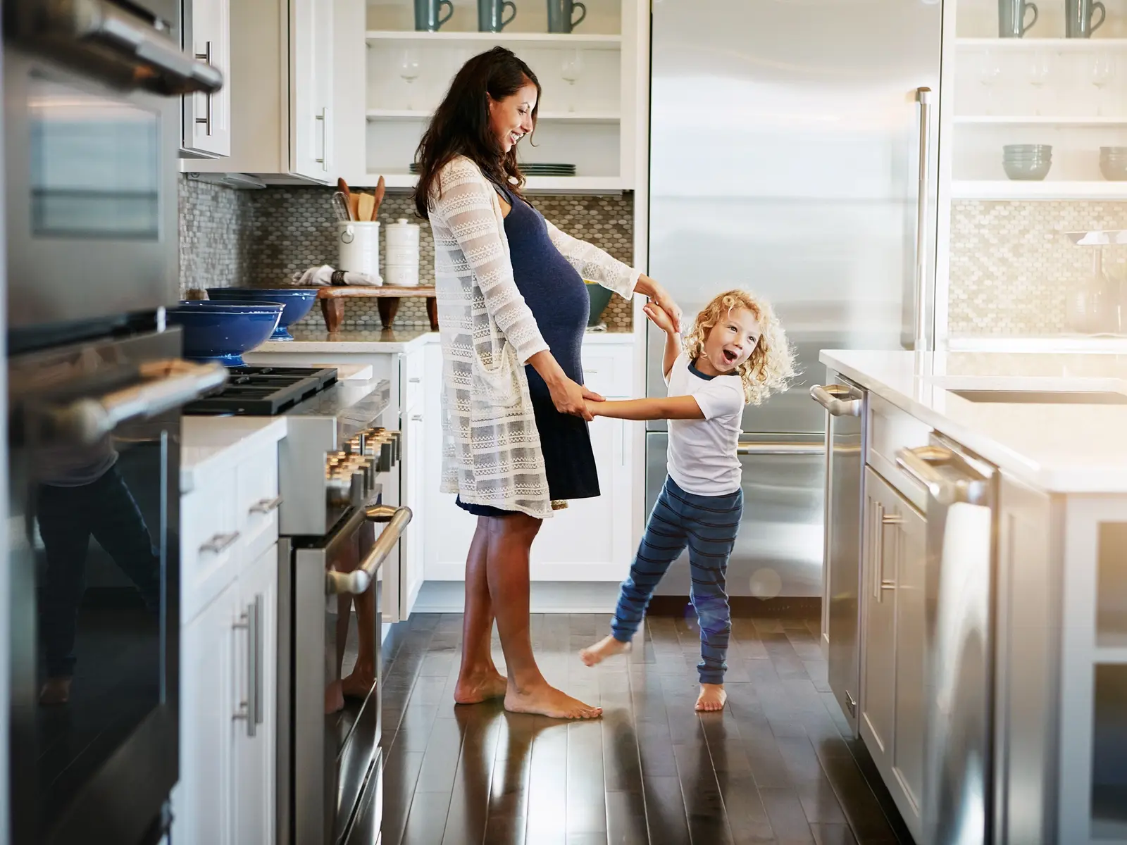 A woman in her third trimester stands in a kitchen with her toddler son