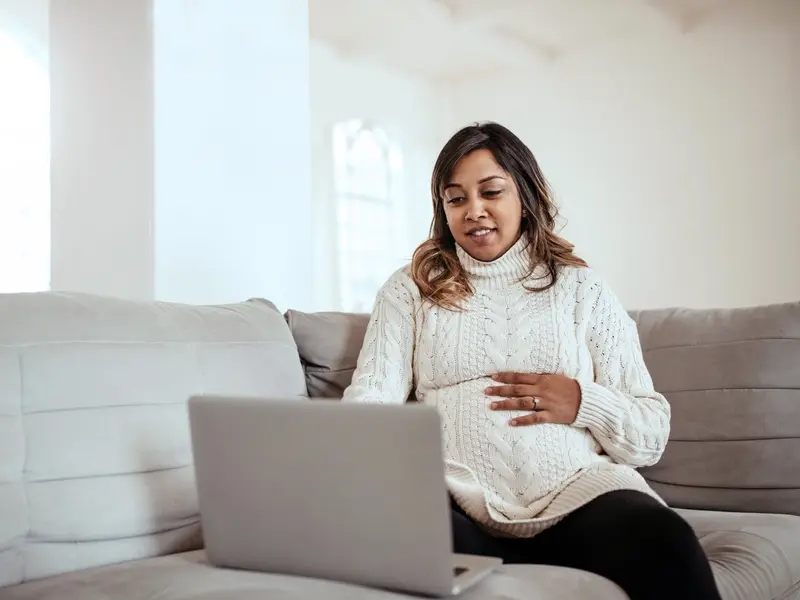 A pregnant woman looking at a laptop computer. 