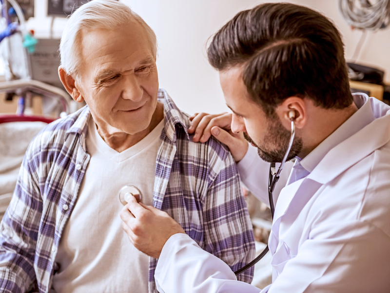 A heart doctor listening to the heartbeat of an older adult man patient 