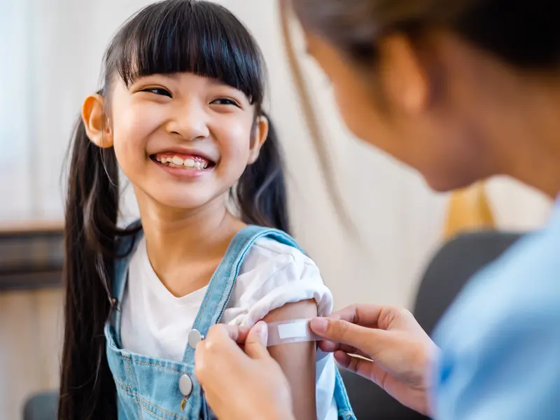 smiling girl getting a Band-Aid on her arm after immunization