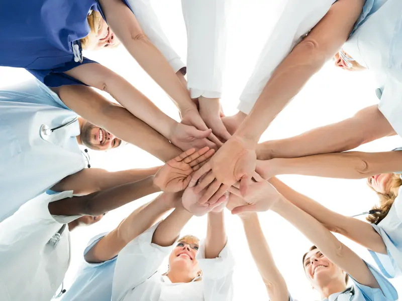 A group of lung care doctors and robotic bronchoscopy medical professionals are standing in a circle, placing their hands together in a team gesture