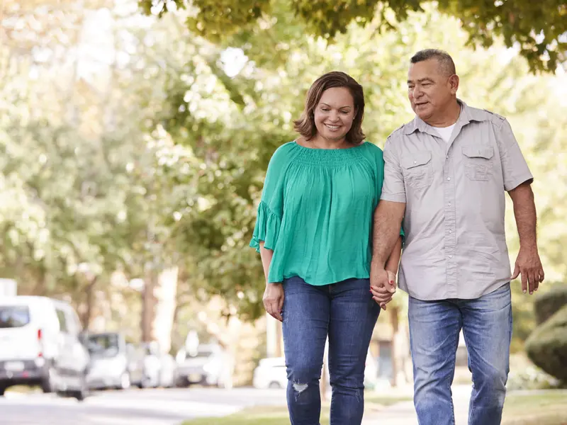 Man recovering from pericarditis treatment and his partner holding hands while enjoying a walk outside on a sunny day