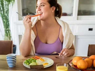 A woman sits at a kitchen table and eats a healthy meal to increase natural GLP-1 hormones in her body