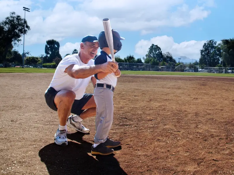 patient on a baseball field teaching his son how to bat after recovering from knee replacement surgery