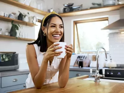 Smiling woman drinks coffee and eats breakfast in the morning