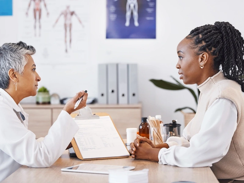 A cardiologist sits at a desk, discussing with a patient how to manage living with heart disease.