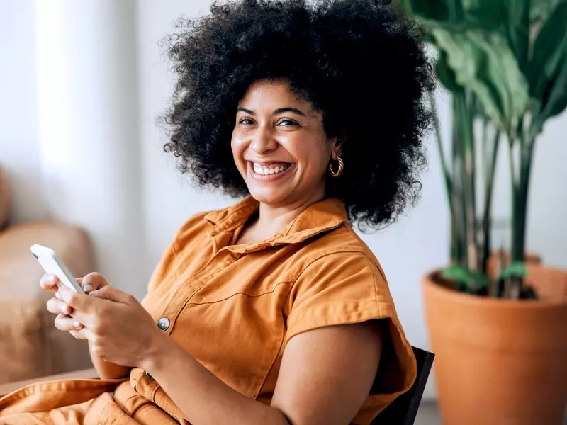 woman sitting in chair, smiling at camera holding phone learning about nipple discharge
