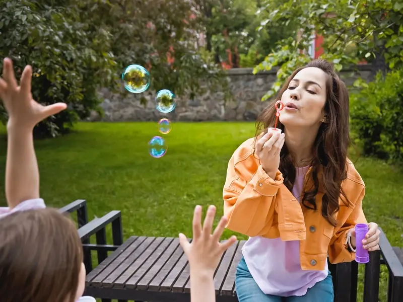 Woman blowing bubble to a child.