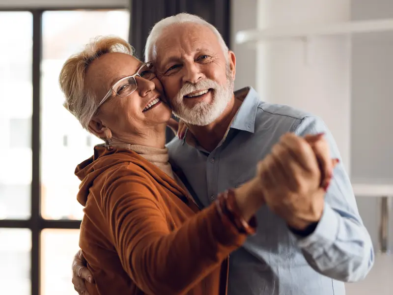 older couple smiling and dancing in their living room