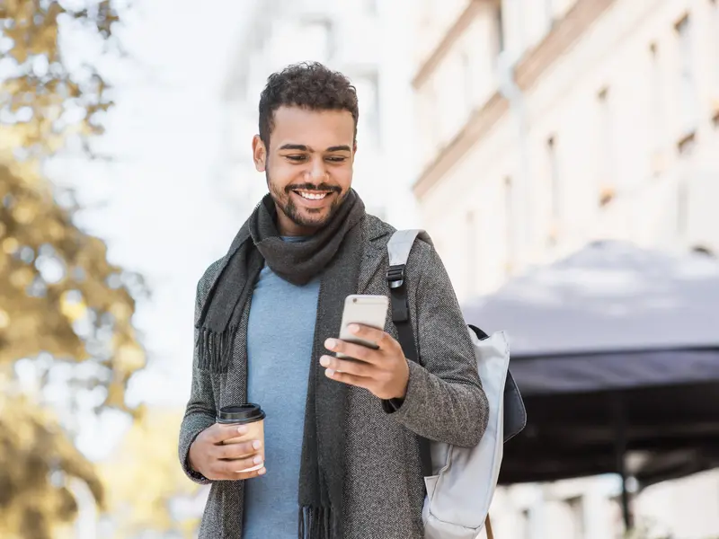 man outside with coffee in one hand and cell phone in the other signing onto BSW Care Guide app