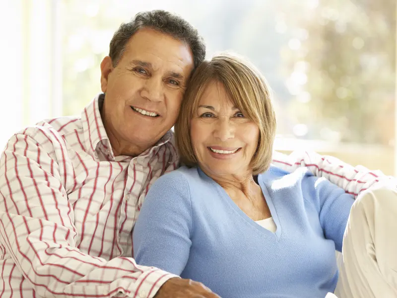 older couple sitting indoors looking and smiling at camera