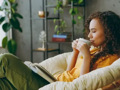 A woman feeling sick before her period, sitting drinking a cup of tea to ease period flu symptoms. 