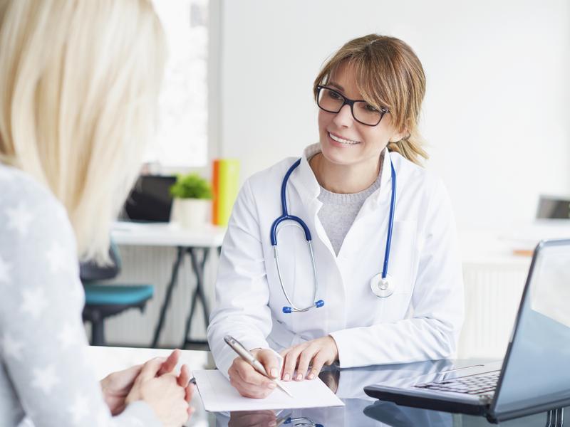 Female cardiologist sitting at a desk with a patient, explaining the risks and management of high cholesterol