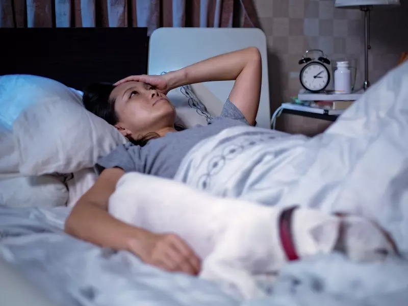 Woman lying awake in bed in the middle of the night, with a hand on her forehead, experiencing insomnia during the menopause transition