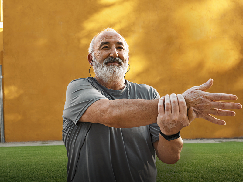 older man stretching outdoors after recovering from treatment for spinal stenosis