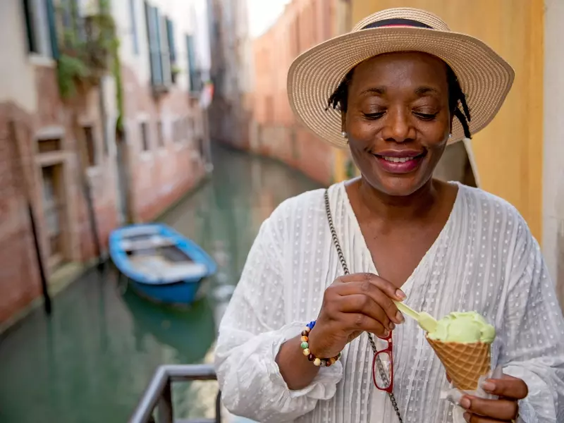 Postmenopausal woman smiling while enjoying gelato by a canal on a sunny day