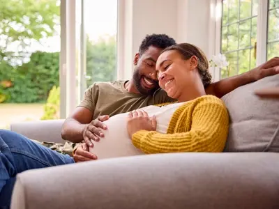 A pregnant woman sitting on the couch with her partner practicing gestational diabetes self care tips