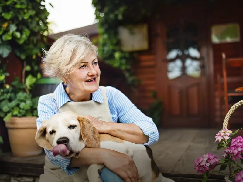 Senior woman with a dog sitting outdoors on farm, resting