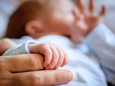 A small newborn baby holding onto its parent’s finger