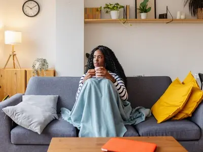 A female sitting on the couch under a blanket experiencing pelvic pain from an ovarian cyst rupture