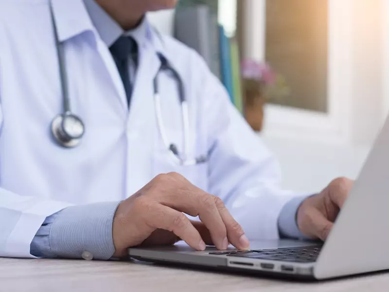 Medical provider seated at a desk, typing medical advice for his virtual care patient on his laptop