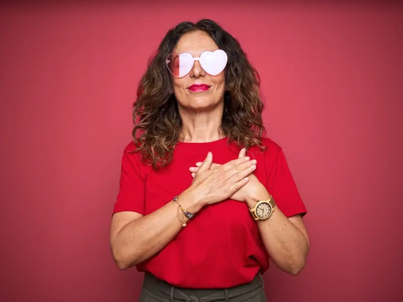 A woman wearing red sunglasses and red shirt with both hands over her heart